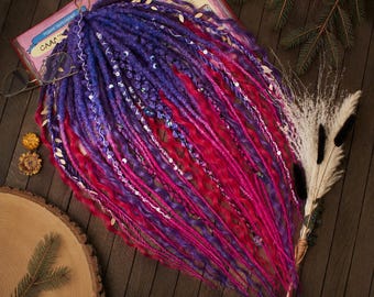 May include: A set of synthetic dreadlocks featuring a vibrant gradient of deep purple, blue, and bright magenta. The strands are a mix of straight and wavy textures, accented with silver-toned charms, beads, and thin decorative wrapping threads.