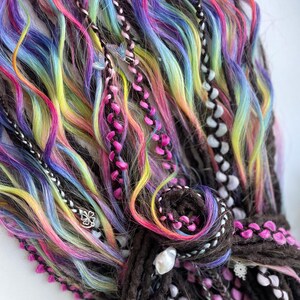 May include: Close-up of colorful dreadlocks with rainbow hues of pink, yellow, blue, and purple. The dreads are accented with braids, beads, and decorative charms. The overall style is vibrant and eye-catching.