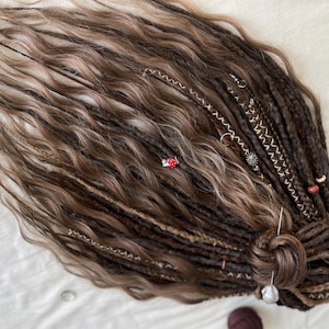 Puede incluir: Un conjunto de rastas sintéticas marrones y rubias con cuentas y abalorios decorativos. Las rastas están atadas juntas en el extremo.