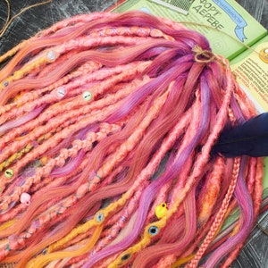 May include: A set of colorful synthetic dreadlocks with beads and a feather accent. The dreadlocks are in shades of pink, orange, yellow, and purple.