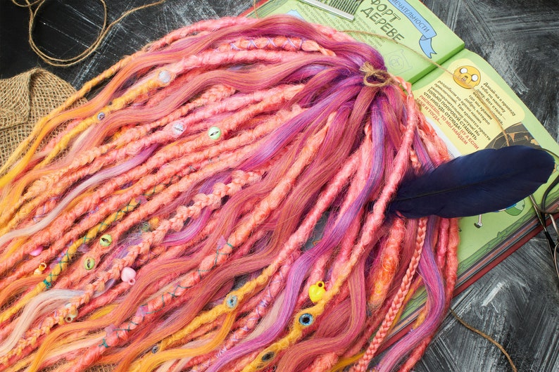 May include: A set of colorful synthetic dreadlocks with beads and a feather accent. The dreadlocks are in shades of pink, orange, yellow, and purple.