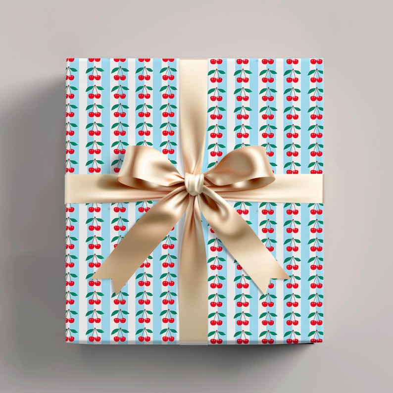 Gift box wrapped in blue cherry-themed paper with red berries and green leaves, tied with a shiny beige ribbon bow, perfect for fun and cheerful gift-giving.