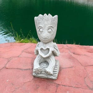May include: A gray concrete statue of a fictional character holding a heart in its hands. The statue is sitting on a red stone surface.