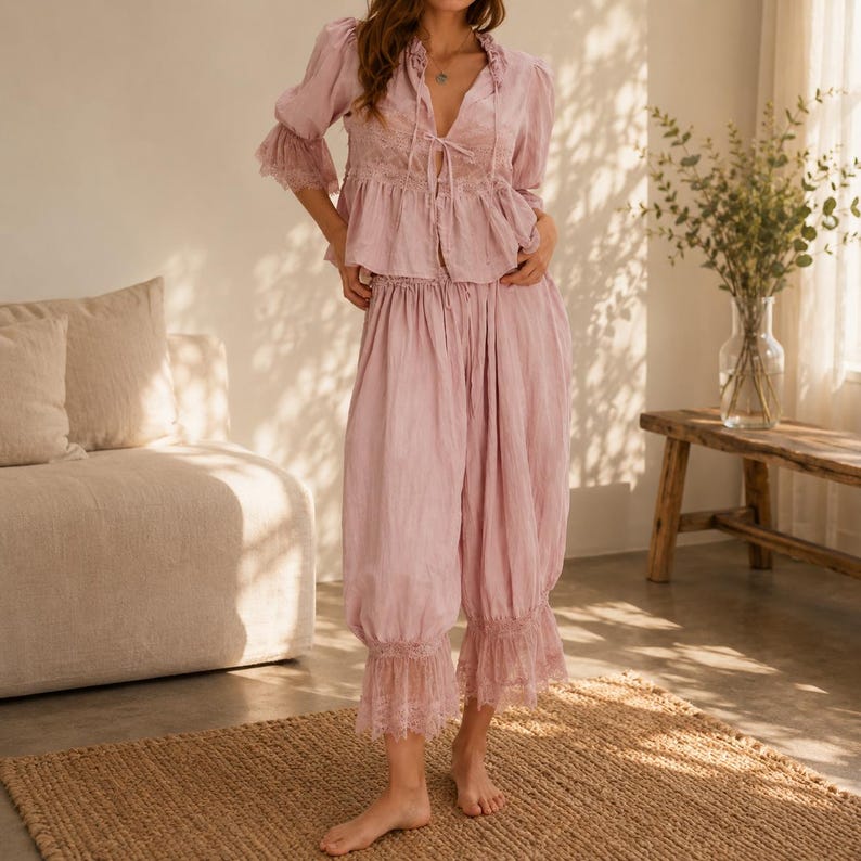 Puede incluir: Un conjunto de dos piezas en color rosa empolvado compuesto por una blusa de manga larga y pantalones cortos a juego. La blusa presenta un escote en V con lazos, detalles de encaje y pu&ntilde;os con volantes. El pantal&oacute;n es de corte holgado.