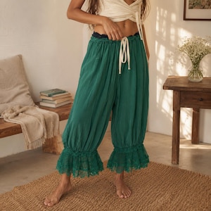 Puede incluir: Pantalones holgados de color verde esmeralda con cintura el&aacute;stica fruncida, cord&oacute;n blanco y ribete de encaje con volantes en el dobladillo. Los pantalones presentan una silueta relajada y voluminosa con un acabado de tela texturizada.