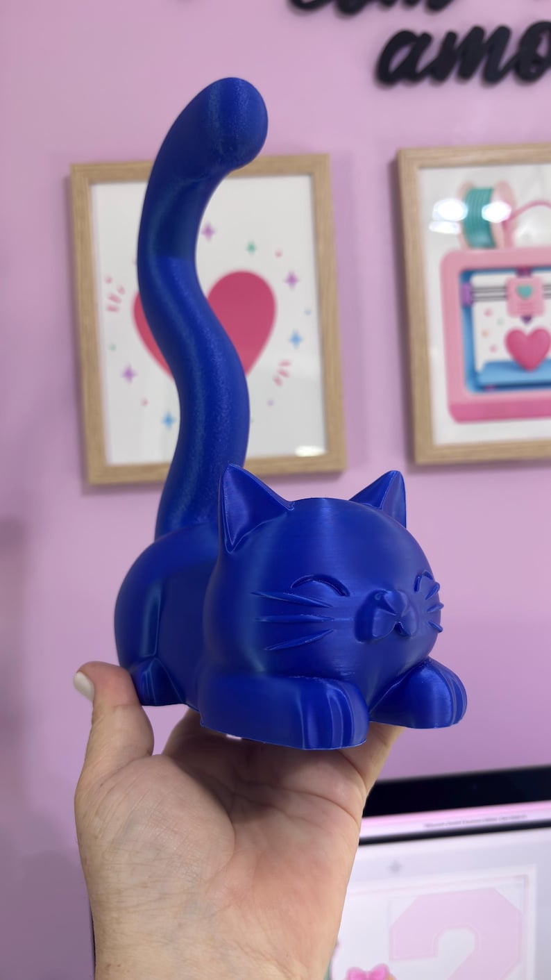 May include: A solid blue cat figurine with a smooth finish, featuring a long, upright tail and a resting posture. The cat has pointed ears, closed eyes, and visible whiskers, with a distinct layered texture characteristic of a 3D printed object.