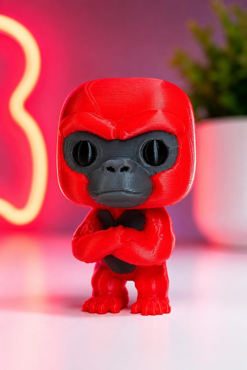 K&ouml;nnte beinhalten: Eine 3D-gedruckte Gorilla-Figur mit leuchtend rotem Kopf, Torso und Gliedma&szlig;en sowie einem dunkelgrauen Gesicht und Brustpanzer. Der Gorilla hat einen gro&szlig;en, abgerundeten Kopf, ausgepr&auml;gte Augenbrauenw&uuml;lste und verschr&auml;nkte Arme vor der Brust.