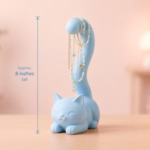 May include: A light blue cat-shaped jewelry holder with a long, curved tail designed to display necklaces. The figure stands approximately 8 inches tall and features a smooth, matte finish with a smiling feline face and pointed ears.