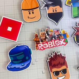 Set of 12 Roblox cupcake toppers featuring popular characters, logos, and icons from the game. Includes layered paper designs with vibrant colors, perfect for gamer-themed birthday parties, cupcakes, and dessert table decor. Ideal for Roblox fans and video game celebrations.