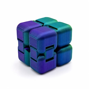 Puede incluir: Un cubo fidget multicolor con un degradado de tonos azules, morados y turquesas. El cubo está compuesto por varios bloques conectados, cada uno con una superficie texturizada. El diseño es geométrico y moderno, adecuado para aliviar el estrés o como juguete de escritorio.