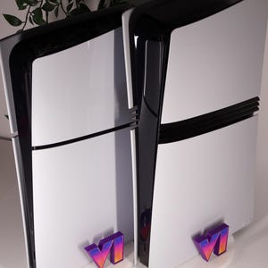 Può includere: Due console di gioco bianche e nere con un logo VI stilizzato davanti. Le console hanno un design elegante con una parte superiore nera e un corpo bianco. Il logo VI è nelle tonalità del viola, arancione e giallo.