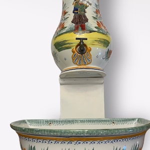 May include: A ceramic wall fountain with a green, yellow, and orange floral design. The fountain has a spout with a brass faucet and a basin with a scalloped edge.