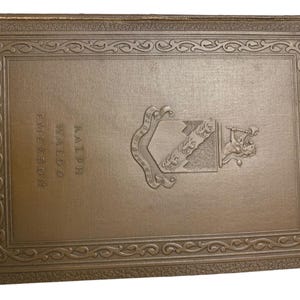 May include: A vintage book with a brown cover featuring embossed text and a decorative border. The book's title is "Ralph Waldo Emerson". A detailed emblem is embossed on the cover, adding to its antique aesthetic.
