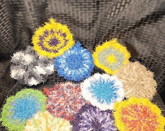 May include: Ten colorful crocheted dishcloths in various colors, including blue, green, yellow, red, purple, and white. The dishcloths are arranged in a circle on a black and white patterned surface.