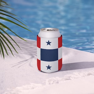 May include: A white can in a red, white, and blue patterned can cooler with two blue stars. The cooler has a checkered design with a blue square in the centre. The background includes a pool and palm fronds.