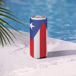 May include: A can cooler displaying the Puerto Rican flag. The design features a blue triangle with a white star, and red and white stripes. The cooler is made of neoprene and is designed to keep drinks cold. It is shown by a swimming pool.