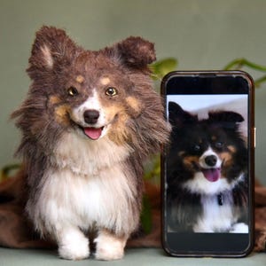 Puede incluir: Un perro de peluche marrón y blanco con una expresión feliz, de pie junto a un teléfono inteligente negro con una foto de un perro similar en la pantalla.