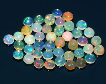 May include: A collection of polished opal gemstones, each displaying a unique play of color. The opals are round, with a mix of vibrant hues including blues, greens, oranges, and pinks. The gemstones are arranged on a dark surface.