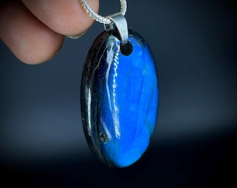 May include: A blue oval labradorite pendant with a silver chain. The gemstone has a polished surface with iridescent blue hues. The pendant is suspended from a silver bail and chain, creating a striking piece of jewelry.
