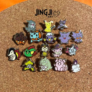 Könnte beinhalten: Eine Sammlung von 17 goldfarbenen Emaille-Pins mit verschiedenen Pokémon-Charakteren. Die Pins sind in einem Kreis auf einem Korkuntergrund angeordnet. Die Pins sind alle in verschiedenen Farben und zeigen verschiedene Pokémon-Charaktere, darunter Pikachu, Glurak, Bisasam, Schiggy und mehr.