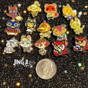 May include: A collection of colorful enamel pins featuring various Animal Crossing characters. The pins have gold-colored borders and are set against a sparkly black background. A US dime is included for size reference. The artist's logo is visible.