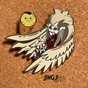 May include: A gold enamel pin featuring a cartoon depiction of a character with large wings, a crown, and a menacing expression. The character is holding a smaller, round character in its claws. A yellow owl with brown accents is perched on the character's wing. The pin has the text "JINGJI ART" at the bottom.