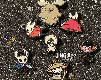 May include: A collection of seven enamel pins featuring stylized cartoon characters, including a tan rabbit-like creature, a red-clad figure, a white-masked knight with a blue cape, and a character with a wide hat, with the text JINGJI ART visible.