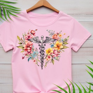 May include: Pink t-shirt with a floral design featuring a silver medical caduceus symbol in the center.