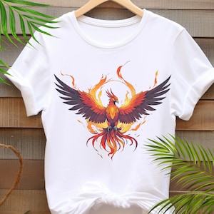 May include: White t-shirt with a graphic of a phoenix rising from flames. The phoenix is orange, red, and yellow with black wings.