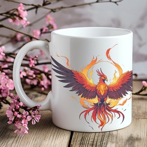 May include: White ceramic mug with a colorful illustration of a phoenix rising from flames. The phoenix is orange, red, and yellow with a white background.