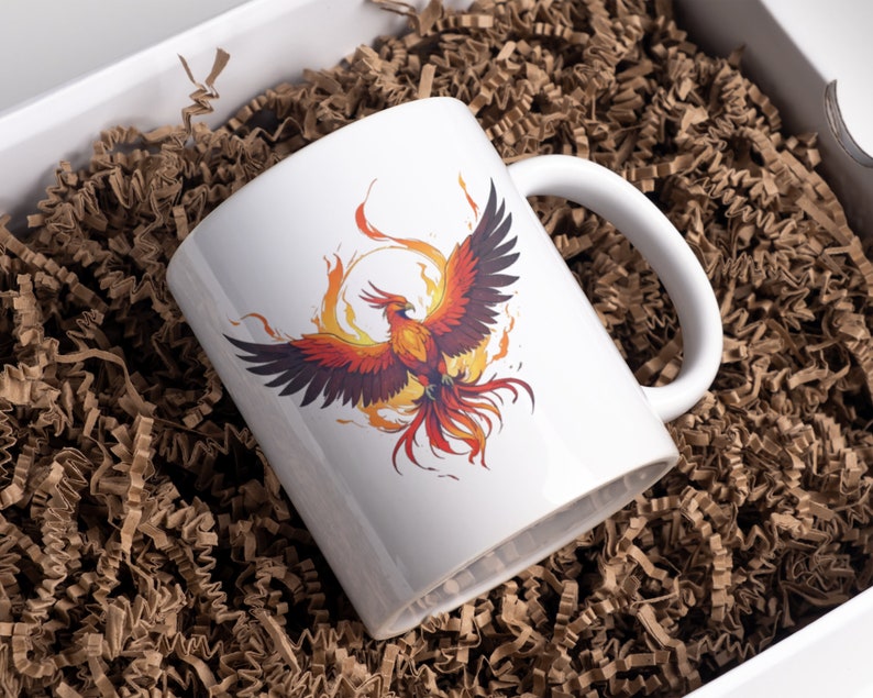 May include: White ceramic mug with a colorful phoenix rising from flames graphic. The mug is in a brown paper gift box.