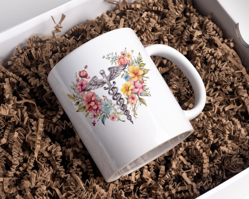 May include: White ceramic mug with a watercolor design of a medical caduceus surrounded by pink, yellow, and blue flowers.