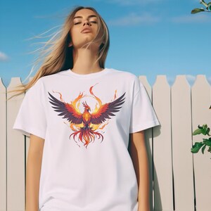 May include: White t-shirt with a graphic of a phoenix rising from flames. The phoenix is orange, red, and yellow with black wings.