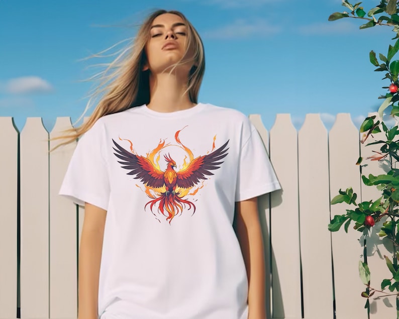 May include: White t-shirt with a graphic of a phoenix rising from flames. The phoenix is orange, red, and yellow with black wings.