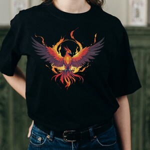 May include: Black t-shirt with a graphic print of a phoenix rising from flames. The phoenix is depicted in shades of orange, red, and yellow, with black wings.