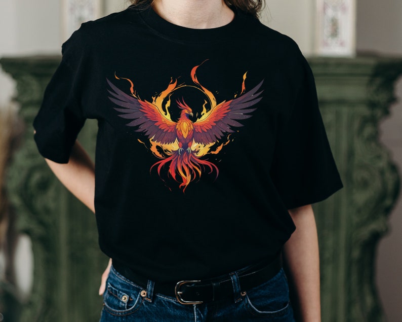 May include: Black t-shirt with a graphic print of a phoenix rising from flames. The phoenix is depicted in shades of orange, red, and yellow, with black wings.