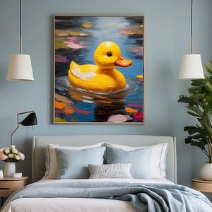 May include: A painting of a yellow rubber ducky floating in a blue pond with colorful leaves. The ducky is facing the viewer with its beak open. The painting is framed and hanging on a blue wall above a bed.