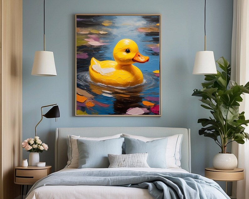 May include: A painting of a yellow rubber ducky floating in a blue pond with colorful leaves. The ducky is facing the viewer with its beak open. The painting is framed and hanging on a blue wall above a bed.