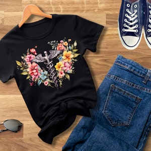 May include: Black t-shirt with a floral design featuring a medical caduceus symbol. The flowers are pink, yellow, and blue.