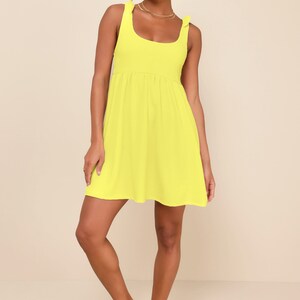May include: A bright yellow sleeveless mini dress with a scoop neck and a tie detail at the shoulders. The dress has a slightly gathered waist and a flowy skirt.