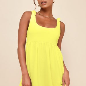 May include: A bright yellow sleeveless mini dress with a scoop neck and tie straps. The dress has a slightly gathered skirt.
