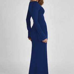 May include: A long, dark blue maxi dress with a V-neckline and long bell sleeves. The dress is fitted through the bodice and flows out to a wide, flowing skirt.