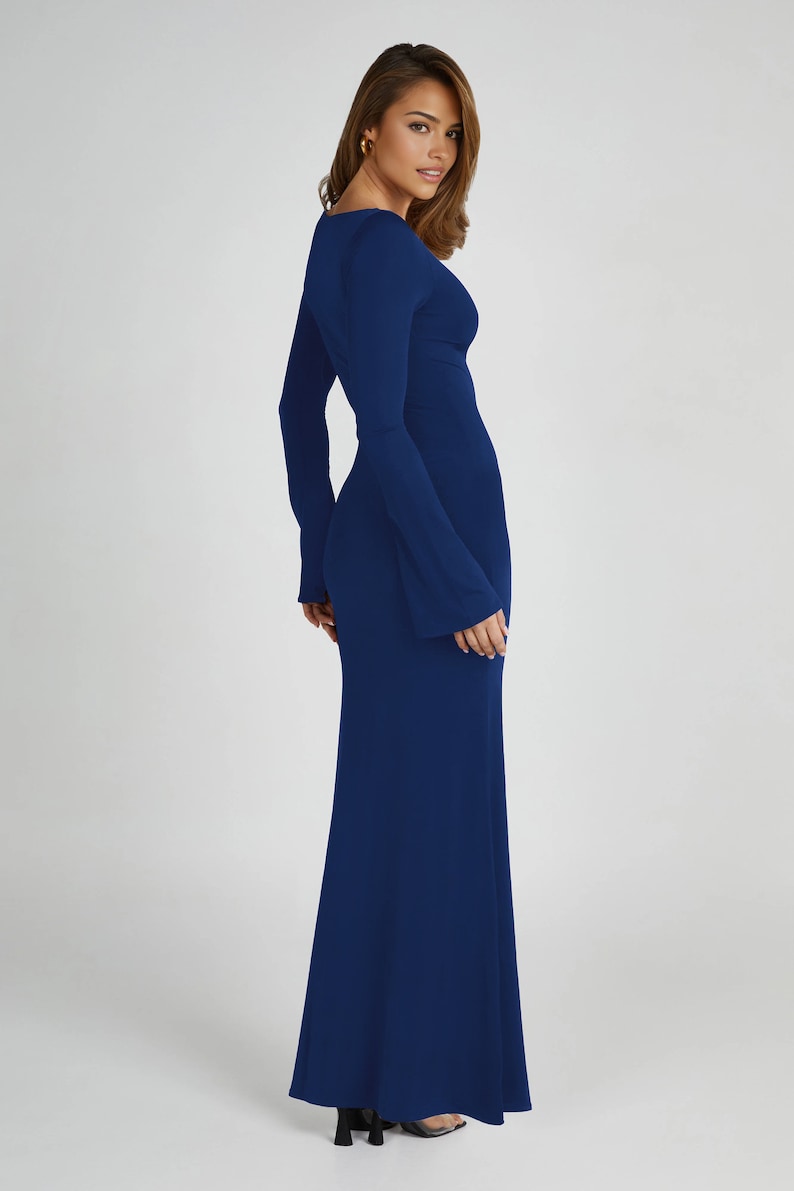 May include: A long, dark blue maxi dress with a V-neckline and long bell sleeves. The dress is fitted through the bodice and flows out to a wide, flowing skirt.