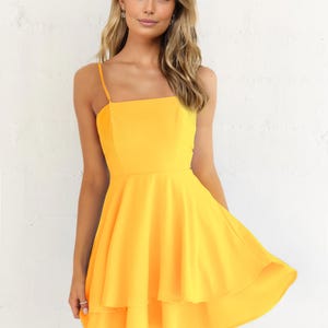 May include: A bright yellow dress with a square neckline and spaghetti straps. The dress features a fitted bodice and a flared, tiered skirt. The fabric has a smooth texture. The dress is knee-length.