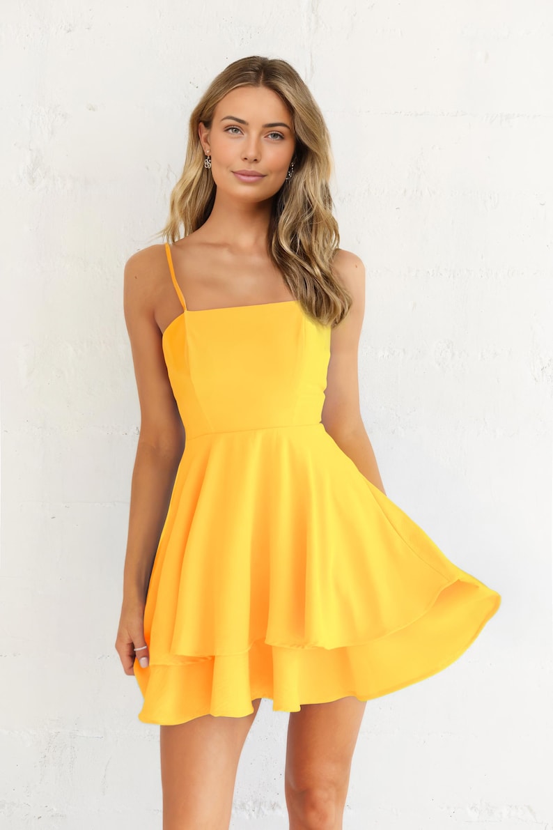 May include: A bright yellow dress with a square neckline and spaghetti straps. The dress features a fitted bodice and a flared, tiered skirt. The fabric has a smooth texture. The dress is knee-length.