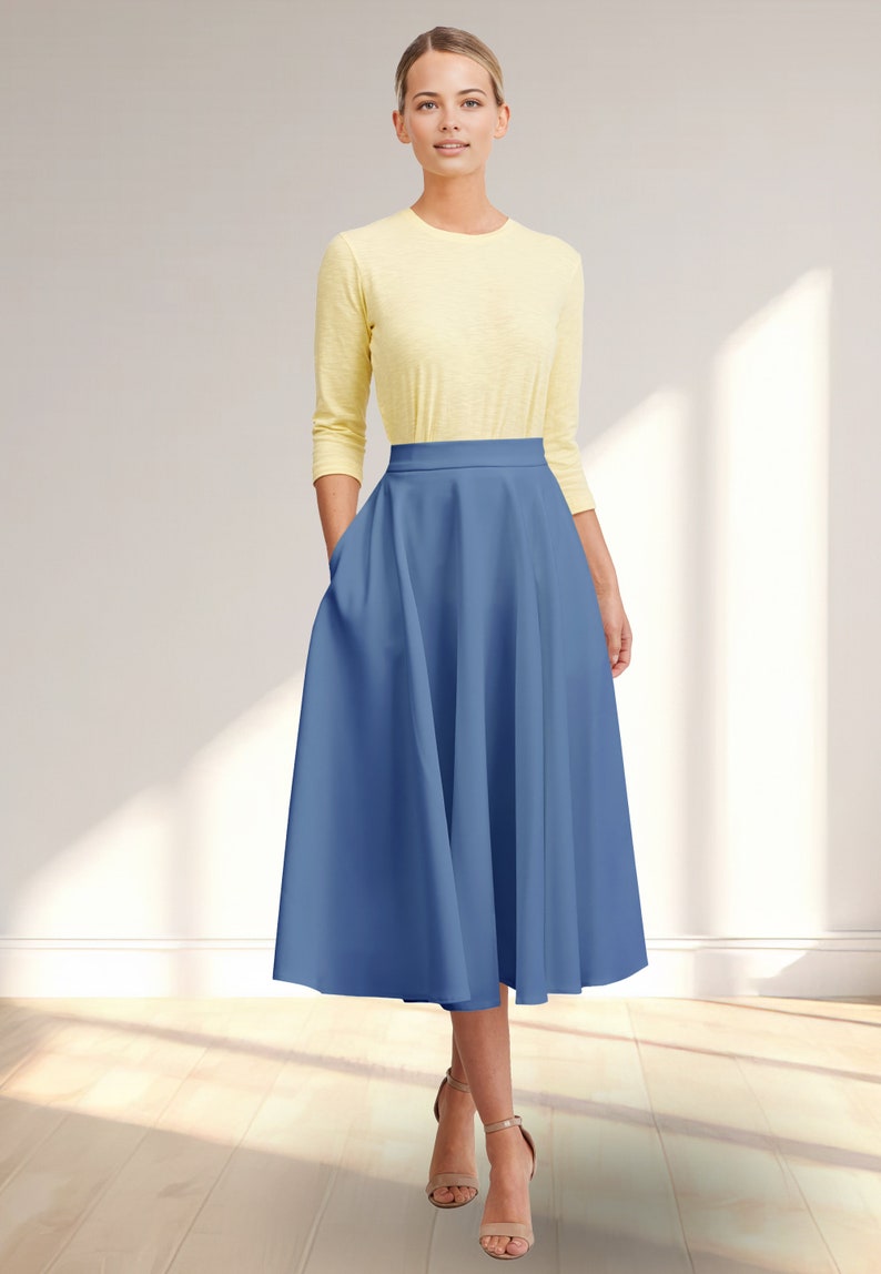 May include: A woman wearing a yellow long-sleeved shirt and a blue midi skirt with pockets. The skirt has a high waist and a full, flowing silhouette.