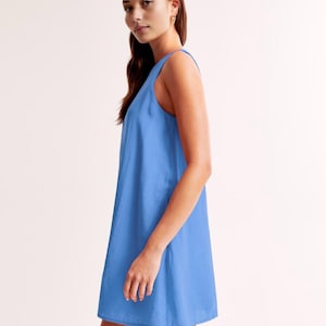K&ouml;nnte beinhalten: Ein &auml;rmelloses, hellblaues Kleid. Das Kleid hat eine einfache A-Linien-Silhouette und reicht bis zur Mitte des Oberschenkels. Der Stoff scheint eine subtile Textur zu haben. Das Kleid wird im Profil gezeigt.