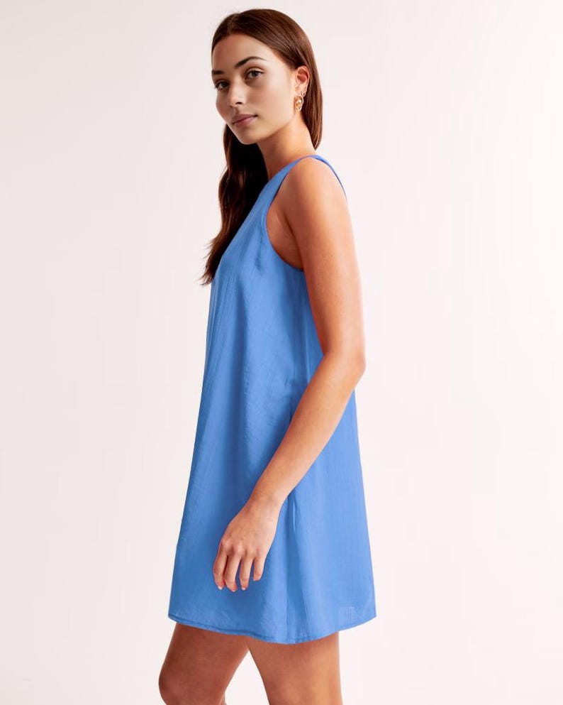 K&ouml;nnte beinhalten: Ein &auml;rmelloses, hellblaues Kleid. Das Kleid hat eine einfache A-Linien-Silhouette und reicht bis zur Mitte des Oberschenkels. Der Stoff scheint eine subtile Textur zu haben. Das Kleid wird im Profil gezeigt.
