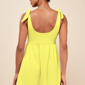 May include: A bright yellow sleeveless mini dress with a scoop neck and tie straps. The dress has a slightly gathered skirt.