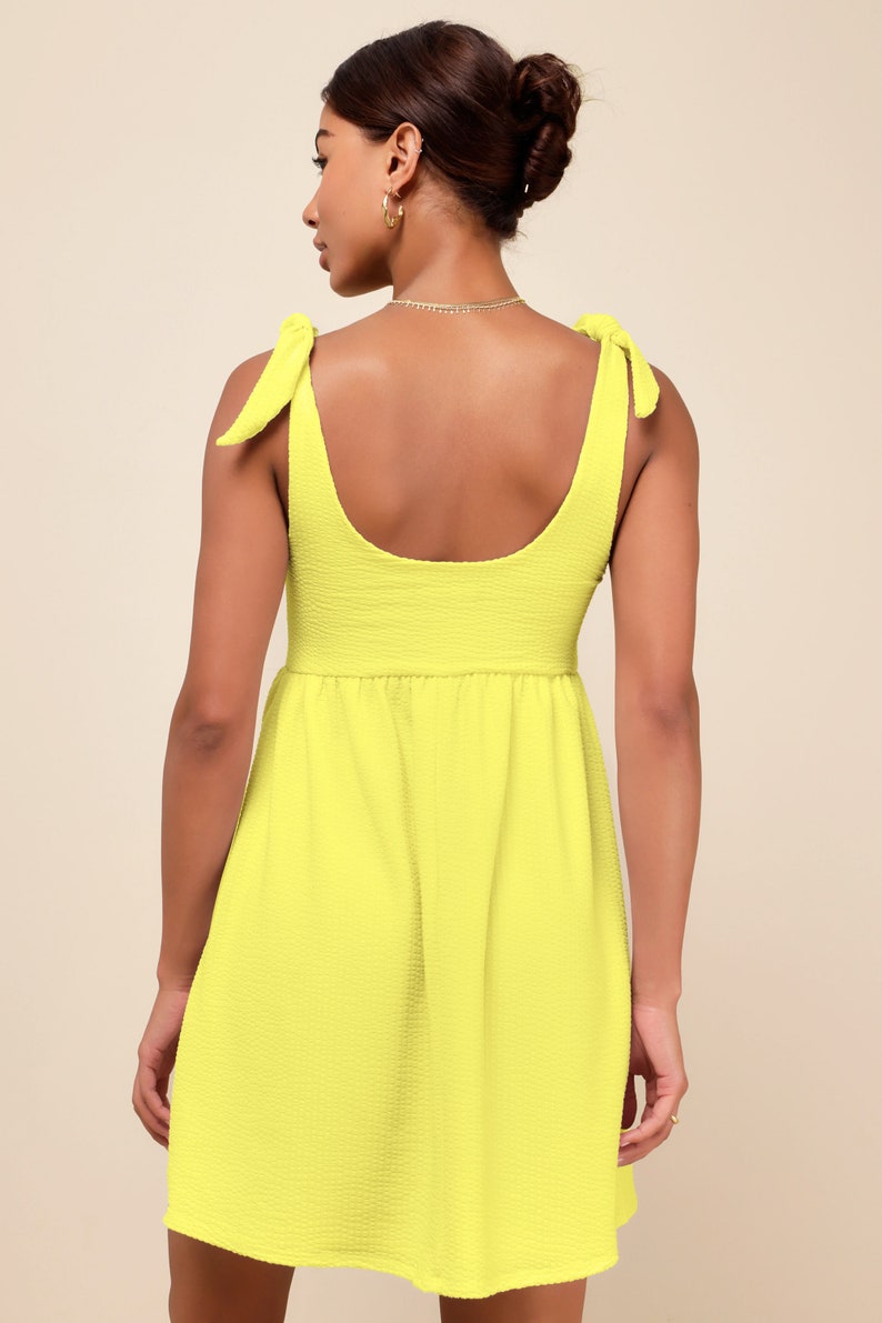 May include: A bright yellow sleeveless mini dress with a scoop neck and tie straps. The dress has a slightly gathered skirt.